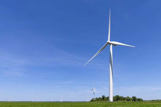 View of modern wind turbines standing in a lush green field under a clear blue sky Toronto, Ontario, Canada.