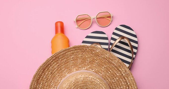 Straw hat, flip flops, sunglasses and sunscreen on pink background, flat lay