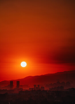 Dramatic red sunrise over hazy Almaty city skyline with bright sun