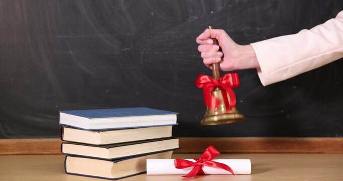 School holidays. Teacher ringing golden bell, books and diploma near chalkboard, closeup