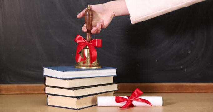 School holidays. Teacher ringing golden bell, books and diploma near chalkboard, closeup