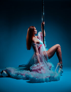 Pole dancer in a lush pink gown posing gracefully on pole in studio