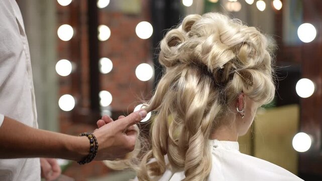Male hairdresser hands styling voluminous blonde hair into an elegant updo. Professional creating a wedding or evening hairstyle for a woman