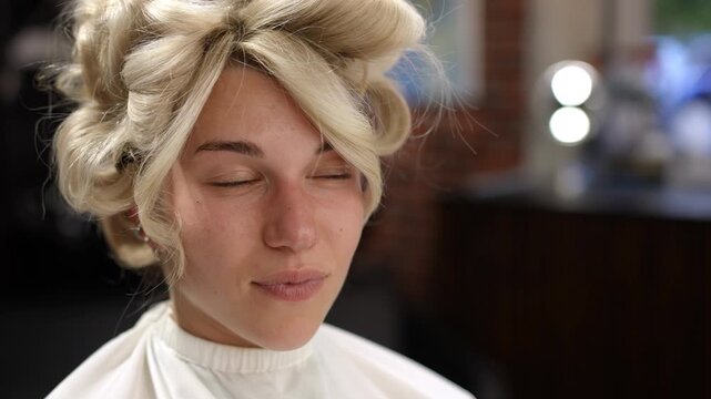 Young beautiful blonde woman with a beautiful evening hairstyle in a beauty salon. She looks at herself in the mirror and smiles enjoying the result