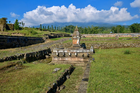 View of the ancient Situs Liyangan temple ruins with terraced stone walls and Mount Sindoro under a blue sky in Temanggung, Central Java, Indonesia.