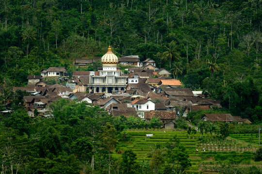 View of the Kebonsari village mosque with its golden dome surrounded by traditional houses and lush green forest in Temanggung, Central Java, Indonesia.