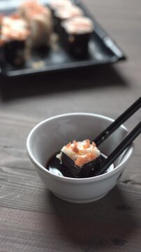 Close up sushi roll dipped in soy sauce with chopsticks on rustic wooden table, Japanese food concept with shallow depth of field.