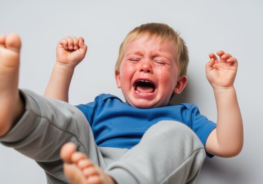 An unhappy little boy with his face contorted in distress and tears pouring down his cheeks while flailing his arms and legs in a state of intense emotional turmoil and frustration