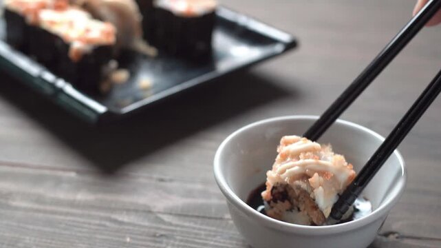 Close up sushi roll dipped in soy sauce with chopsticks on rustic wooden table, Japanese food concept with shallow depth of field.