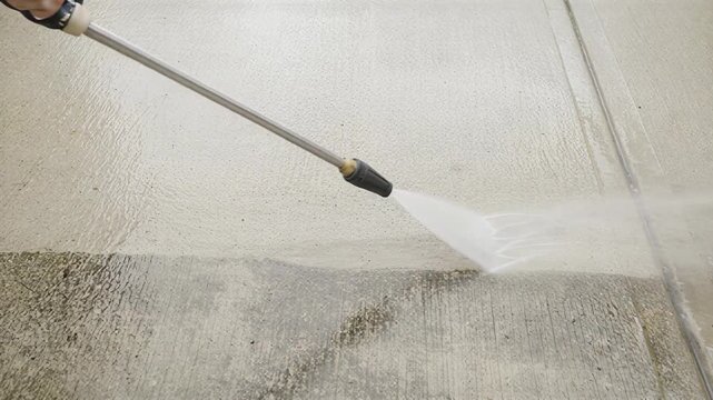 High-pressure water spray cleaning a dirty concrete surface, removing grime and stains effectively