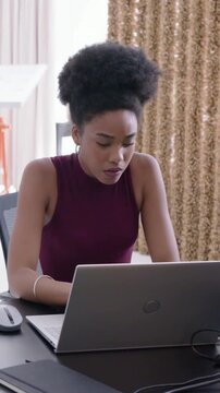 Vertical video: Reading paper maroon-top woman entering data at home with laptop, external keyboard