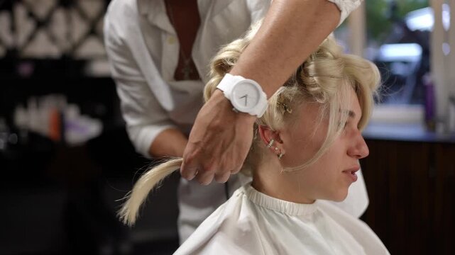 Young woman sitting in a beauty salon chair while a professional stylist uses a curling iron to create an elegant and voluminous hairstyle