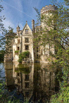 Les Trois-Moutiers, France - 13 April 2024: View of the ruined Chateau de la Mothe-Chandeniers reflected in its moat, surrounded by lush green trees under a clear blue sky.