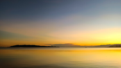 Obraz premium Minimalist sunrise over calm ocean water with island silhouettes and soft golden reflections beneath a clear morning sky. Ideal to illustrate travel, wellness, and web banners.