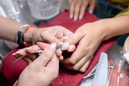 Manicurist trimming cuticles on client's fingernails in salon
