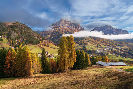 Majestic mountain peak with colorful autumn larch forest and rolling clouds near Colle Santa Lucia, Dolomites, Italy.