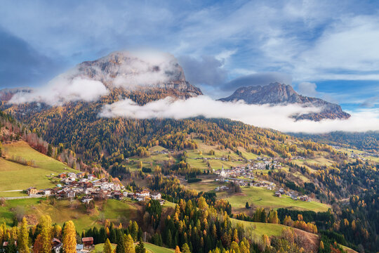 Majestic mountain peak with colorful autumn larch forest and rolling clouds near Colle Santa Lucia, Dolomites, Italy.