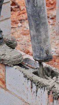 Construction worker operates concrete pump to compact fresh concrete on block wall at building site.