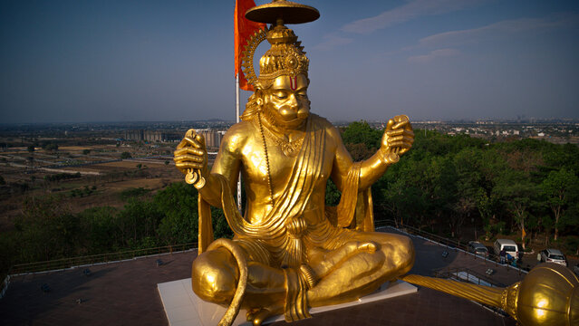 Indore, India - 08 May 2025: View of the massive golden Lord Hanuman statue at Pitra Parvat, seated with cymbals against a clear sky and the Indore city skyline.