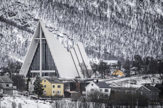 Tromso, Norway - 11 March 2026: View of the Arctic Cathedral with its iconic triangular architecture against a snowy mountain backdrop and residential houses.