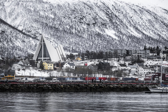 Tromso, Norway - 11 March 2026: View of the Arctic Cathedral with its modern triangular architecture set against snow-covered mountains and a waterfront with people walking.