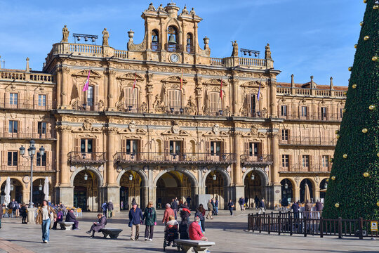 Salamanca, Spain - 01 December 2025: View of the baroque Town Hall in Plaza Mayor with a large Christmas tree and people walking across the square under a clear blue sky.