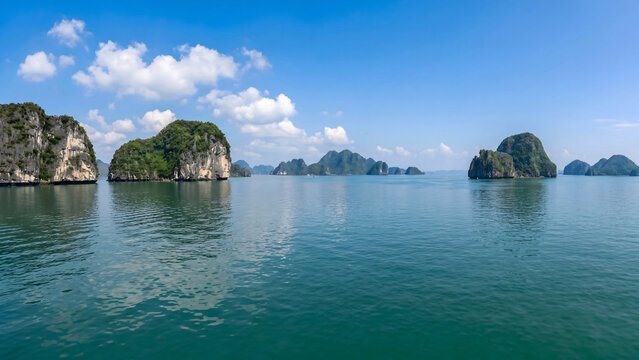 Lush green limestone karsts rise from calm turquoise waters under a blue sky