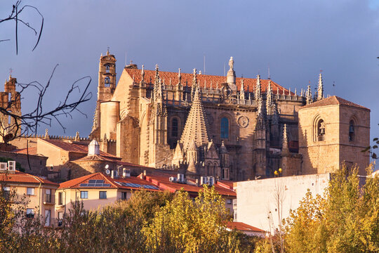 Plasencia, Spain - 02 December 2025: View of Catedral Nueva de Plasencia with its ornate Gothic architecture, stone bell tower, and red-tiled roofs under a soft sky.