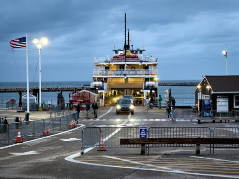 Edgartown, United States - 14 May 2026: View of a car disembarking from a large ferry at the Martha's Vineyard terminal under a twilight sky with the American flag waving.