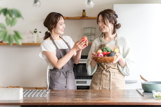 A young Asian woman in an apron holding vegetables in a kitchen (cooking class, cooking school)