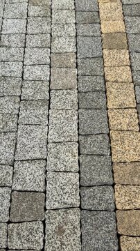 Vertical cinematic pan of elegant grey and yellow granite paving stones texture. Professional cobblestone pavement background with detailed granite rock pattern structure.