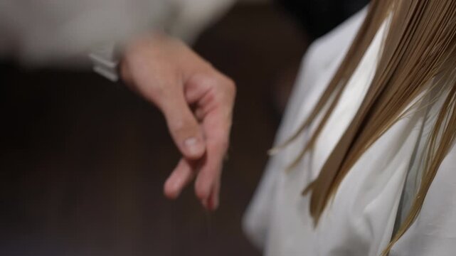Close-up of a hairdresser's hands skilfully cutting the ends of a client's long, wet blonde hair using a comb and scissors in a salon