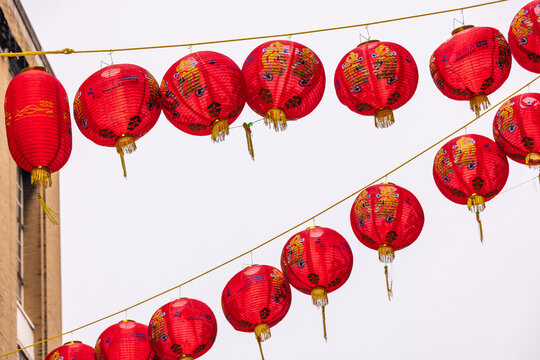 London, United Kingdom - 12 May 2025: View of red Chinese lanterns with golden dragon patterns hanging on strings against a pale sky in Chinatown.
