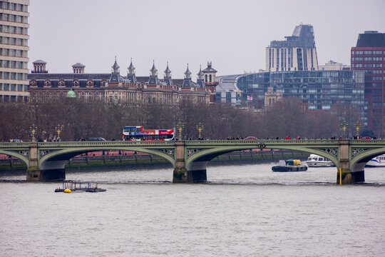 London, United Kingdom - 12 May 2025: View of Westminster Bridge with a red double-decker bus and pedestrians crossing the River Thames under an overcast sky.