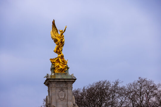 London, United Kingdom - 12 May 2025: View of the golden Victoria Memorial statue standing atop its stone pedestal against an overcast sky and bare trees.