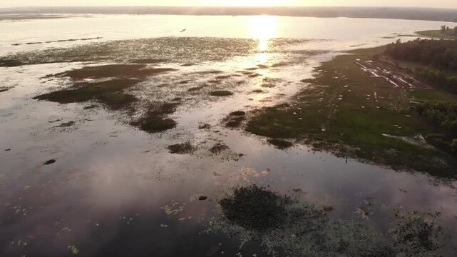 Aerial view of a serene wetland landscape with calm water and grassy areas at sunset.