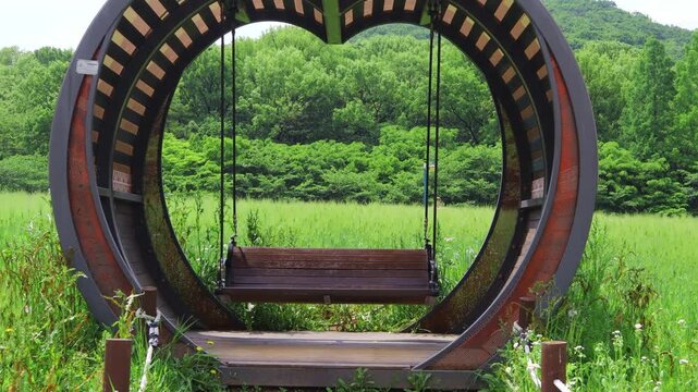 A swing is moving on the meadow spread out in the park.공원에 펼쳐진 초원위에 그네가 움직이고 있습니다.