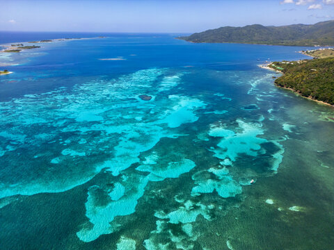 Aerial view of the vibrant coral reefs and turquoise waters along the lush coastline of Guanaja, Bay Islands Department, Honduras.
