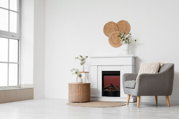 Fototapeta premium Interior of light living room with blooming branches in vases, fireplace and armchair