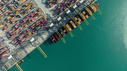 Aerial drone shot of crane loading containers onto cargo ship at Laem Chabang Port. © Nutchanart