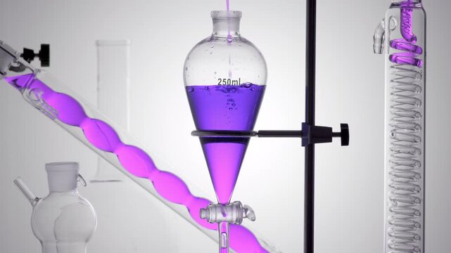 Lab setup with clear violet fluid poured in a thin stream into a separatory funnel, making bubbles underwater and flowing down a lab condenser coil on a curved grey base
