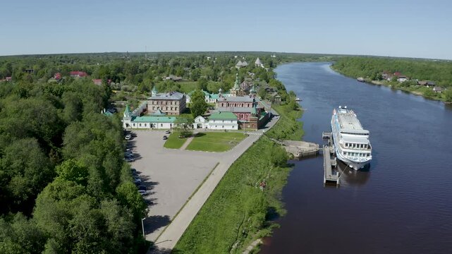Tilt down aerial shot of cruise ship on Volkhov river nearby Nikolsky monastery on sunny summer day. Staraya Ladoga, Russia.