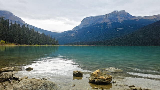 Scenic view of turquoise glacial lake with rocks in the foreground and majestic mountains