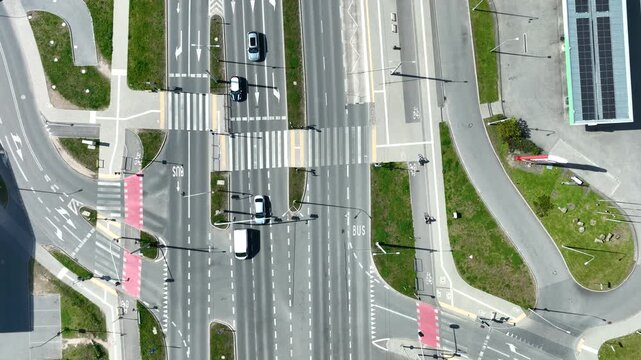Cinematic aerial topdown perspective of a modern urban road junction in Gdynia, featuring marked bike lanes, pedestrian crossings, and light vehicle traffic.