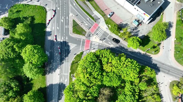 Cinematic aerial topdown shot of a modern urban road intersection with crosswalks and green trees in Gdynia, Poland. Suitable for urban planning and sustainability themes.