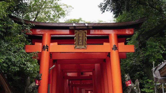 Large red torii gate with gold Inari Okami plaque and kitsune fox statues marking the tunnel entrance at Fushimi Inari Kyoto