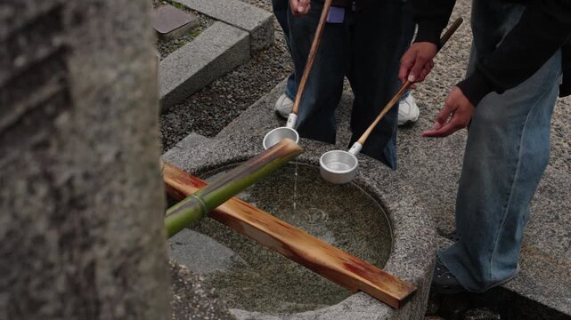 Visitors holding wooden handled ladles over a round stone temizuya water basin during purification ritual at a Japanese shrine