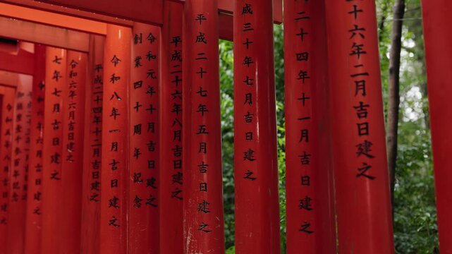 Rows of red torii gate pillars densely covered in black kanji inscriptions at Fushimi Inari Taisha in Kyoto