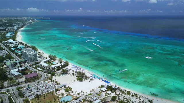 Drone descends over Seven Mile Beach, showing turquoise water, white sand, boats, and Grand Cayman coastline