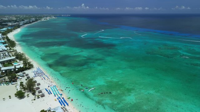 Drone ascends and pulls back over Seven Mile Beach, showing turquoise water, white sand, boats, and Grand Cayman coast